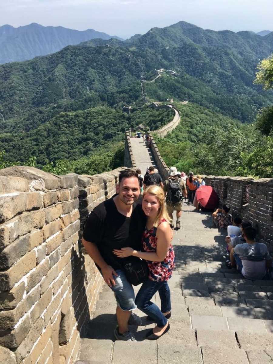 Husband and wife stand arm in arm on Great Wall of China on their trip to adopt their son