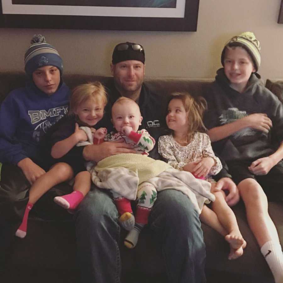 Father sits on couch with his three biological kids and two adopted kids