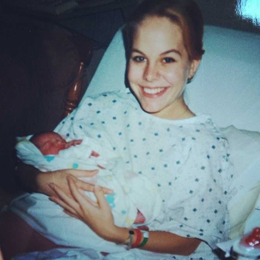 Mother lays in hospital bed smiling as she holds her newborn in her arms