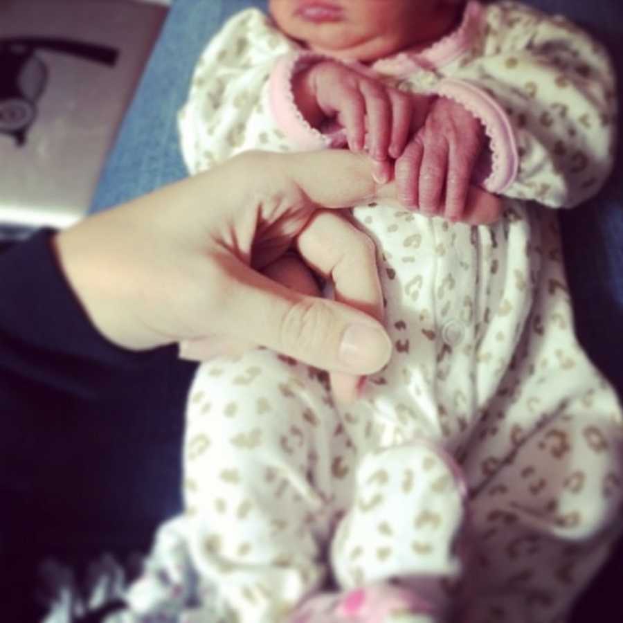 Newborn girl holds finger of adoptive mother