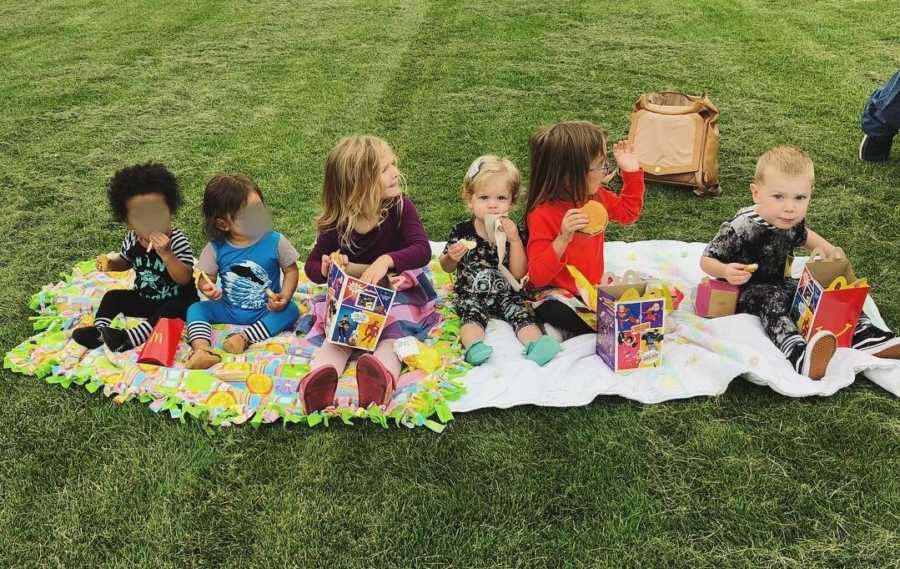 Young kids sit on blankets outside eating Happy Meals