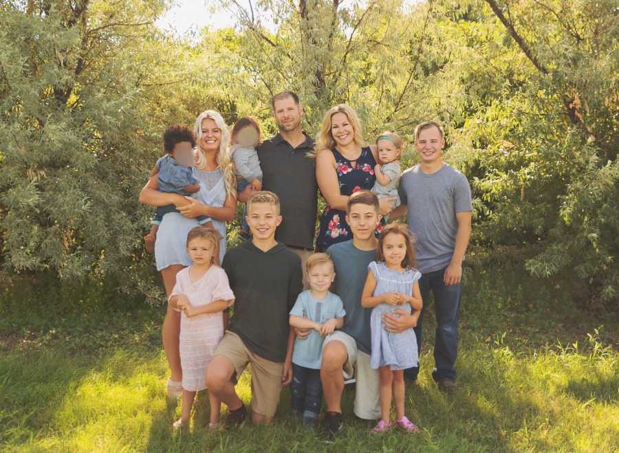 Husband and wife stand with their nanny, three biological kids, two adopted kids, and four foster kids