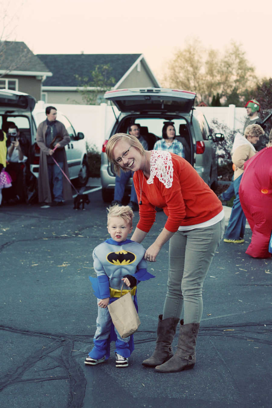 Adopted little boy in Batman costume smiles beside his birth mother in parking lot