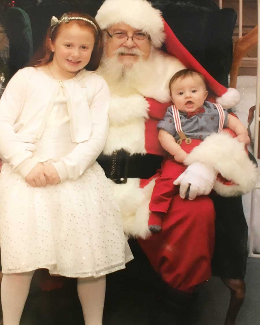 Little girl sits on mall Santa's lap with her baby brother