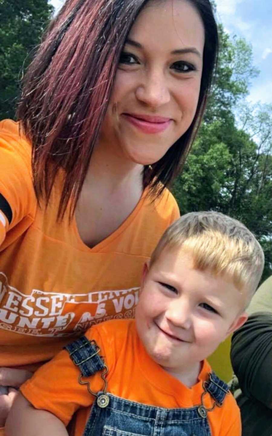 Mother smiles in selfie with young son smiling on her lap