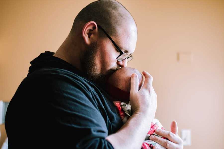 Father holds baby girl with chest as he kisses her forehead