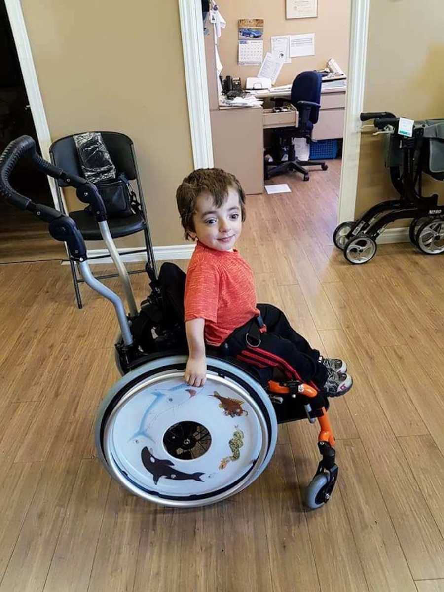 Little boy who has had over 14 surgeries in his life sits in wheelchair smiling