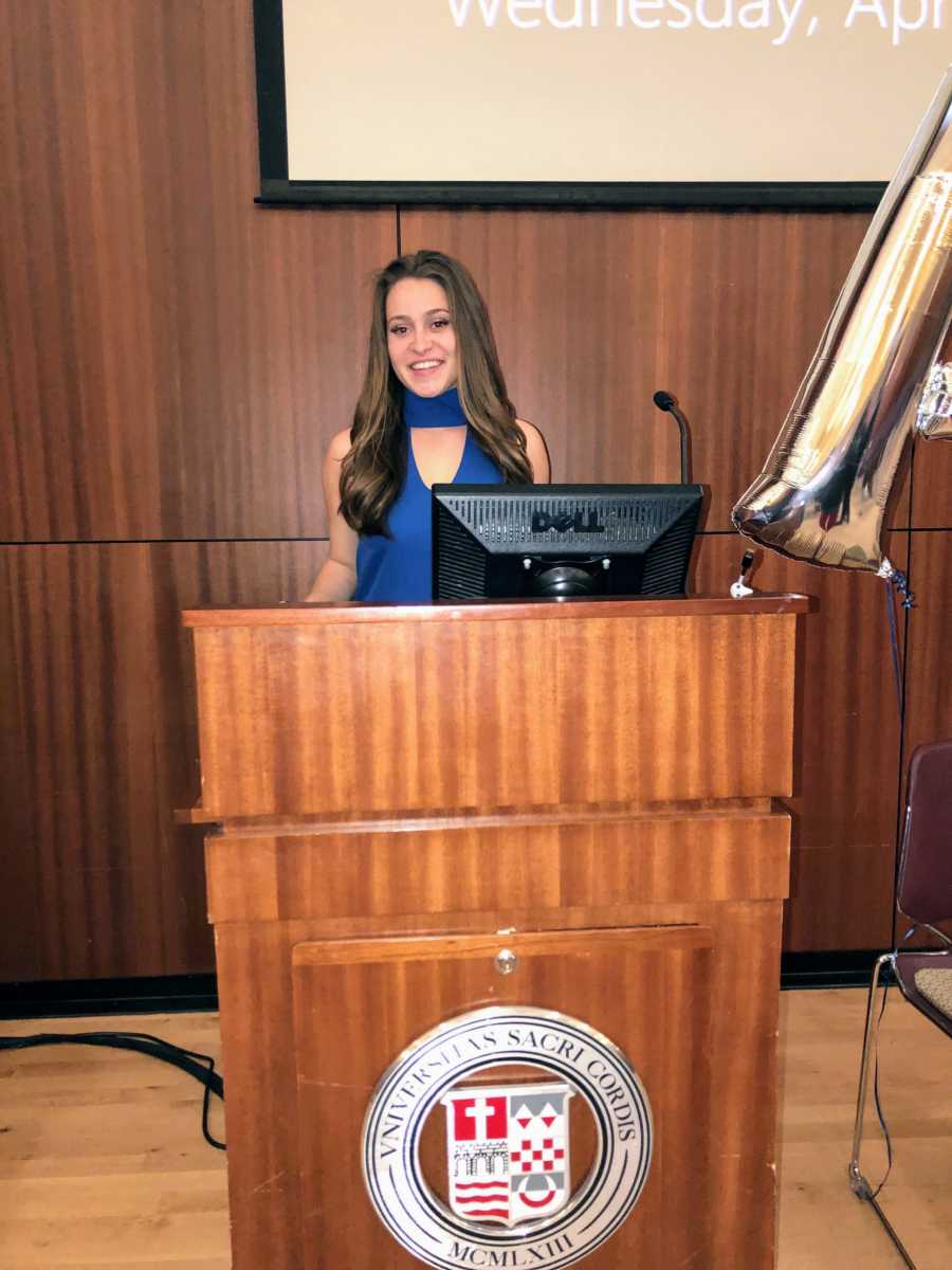 Woman in graduate school standing at podium smiling 