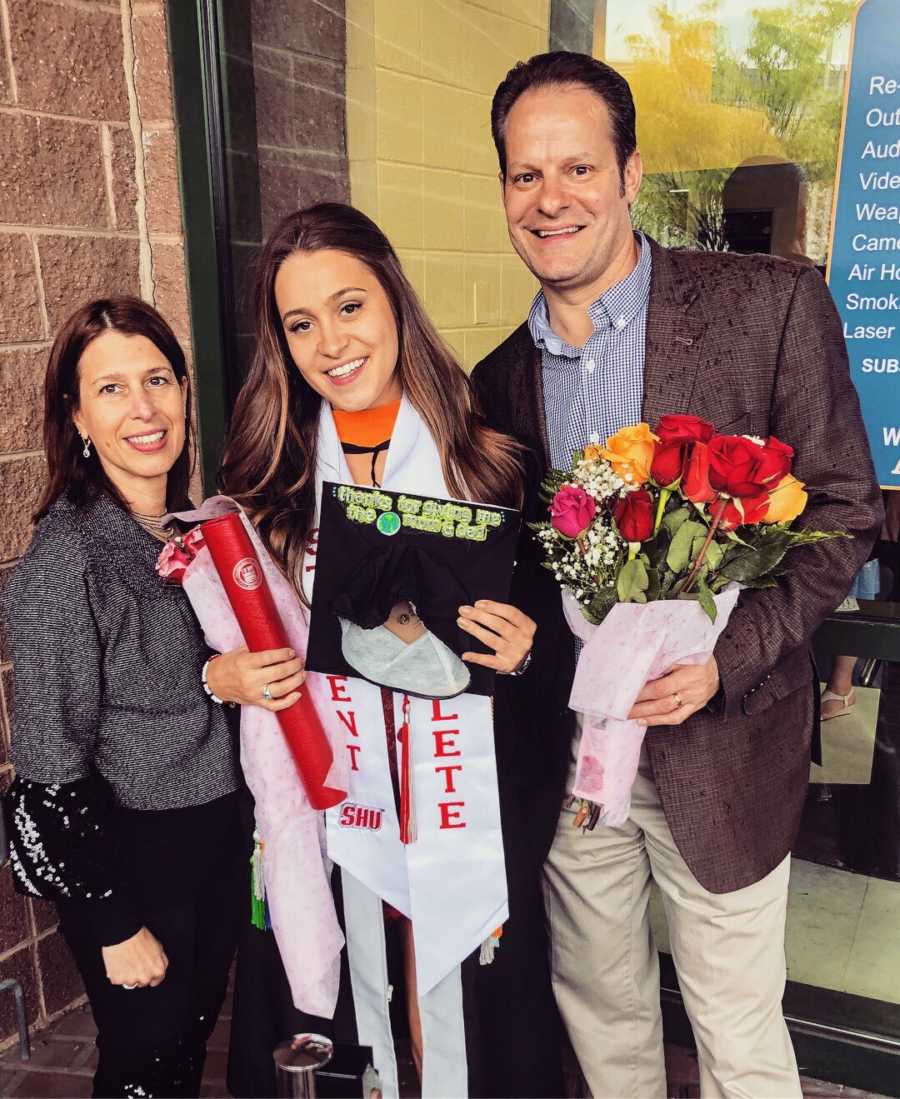 Young college graduate with post graduate depression stands smiling with parents at graduation