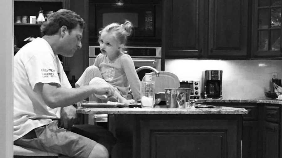 Father sits at island in kitchen eating food while daughter sits on countertop looking at him