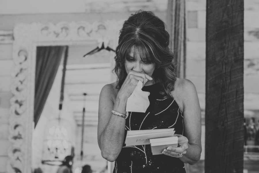 Mother of groom stands crying while looking at card in her hand