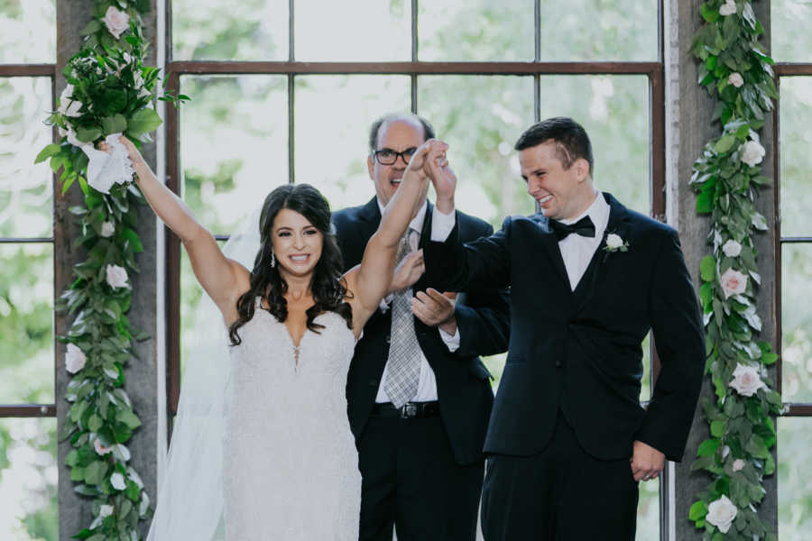 Bride and groom who recovered from car crash stand smiling at altar with officiant behind them