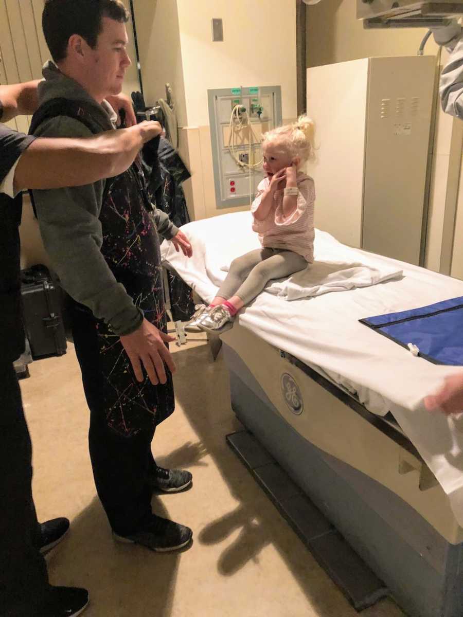 Little girl who ate magnet sits in hospital room after receiving x-ray as her father stands beside her