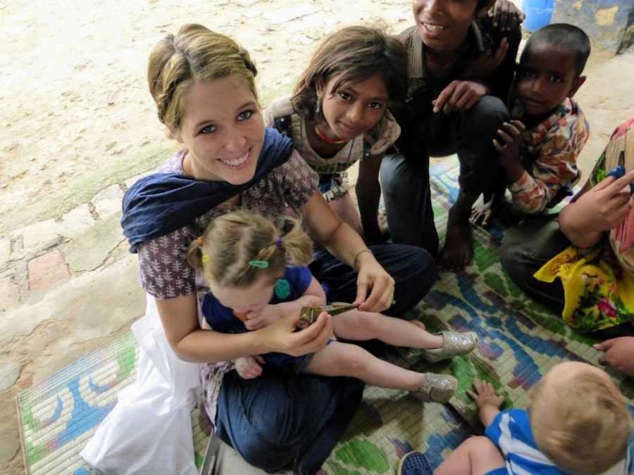 Woman sits on ground with daughter in her lap beside children at children's care center in India