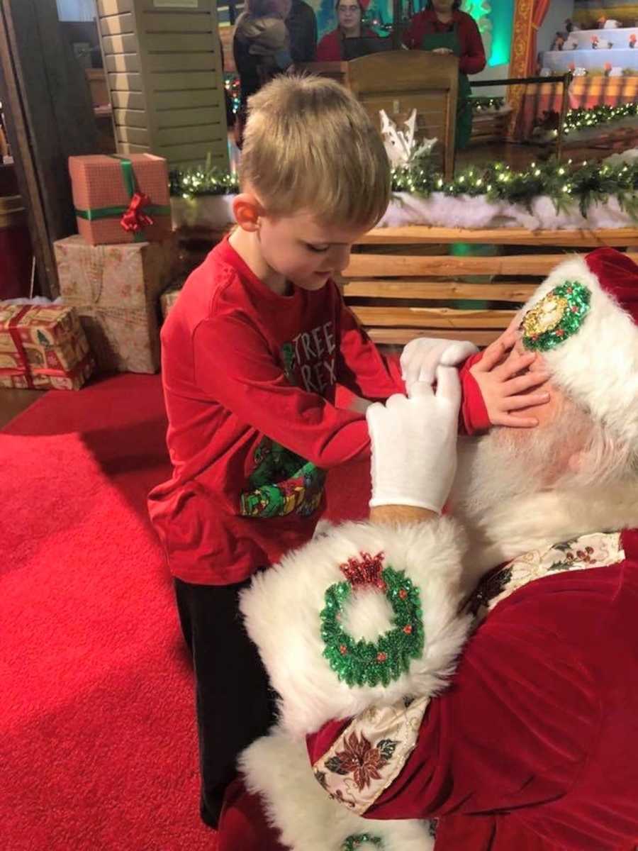 Young boy who is blind and autistic stands holding mall Santa's face who is sitting on ground