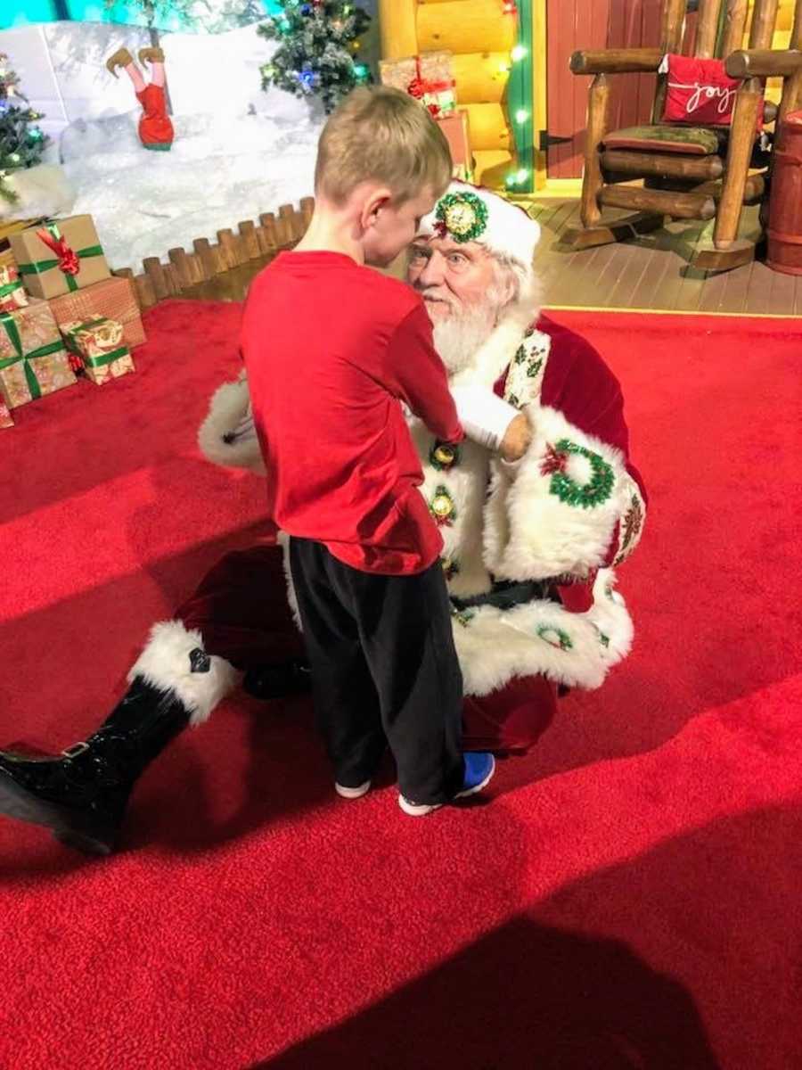 Santa sits on floor holding hands of young boy who is blind and autistic