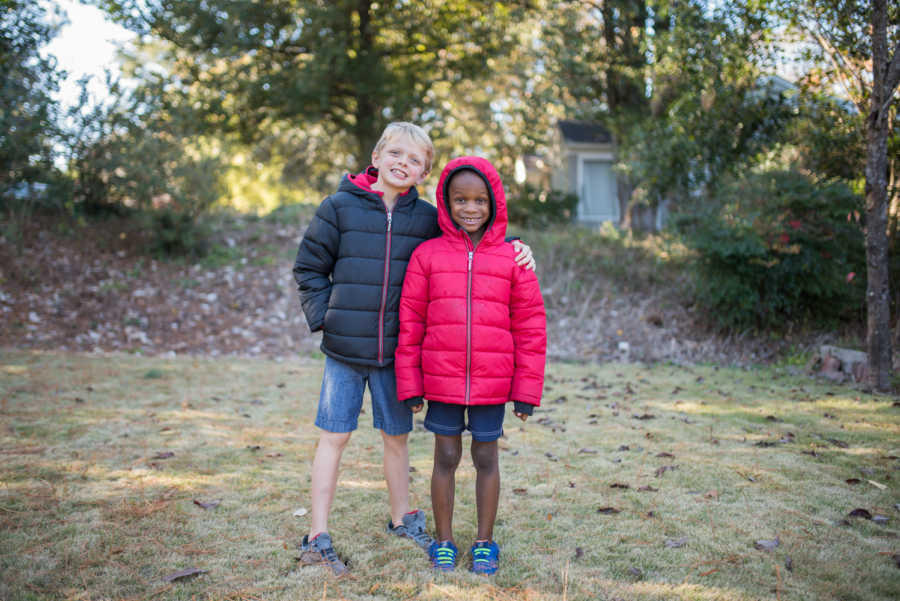 Young boys standing outside arm in arm in down coats and shorts