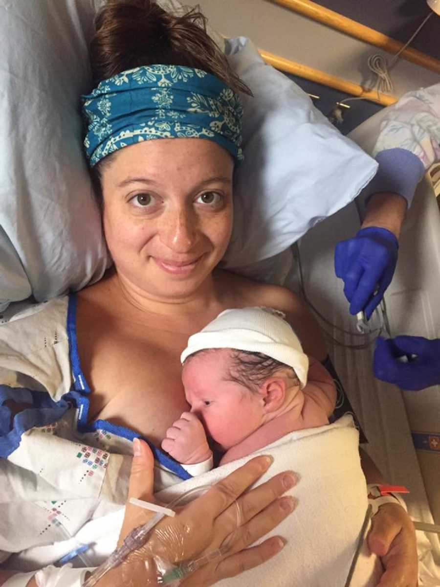 Mother lays in hospital bed smiling with newborn laying on her chest