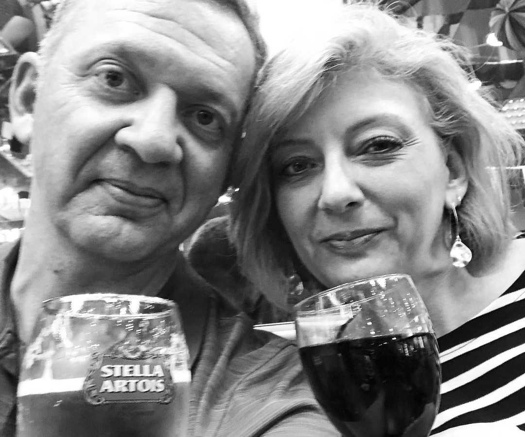 Husband and wife smile in selfie holding up drinks