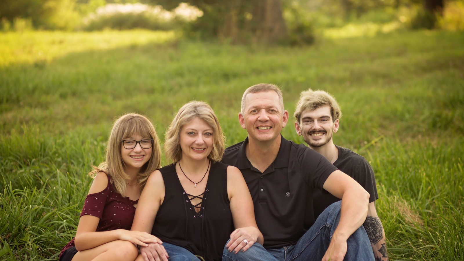 Husband and wife sit on ground outside with their daughter and son