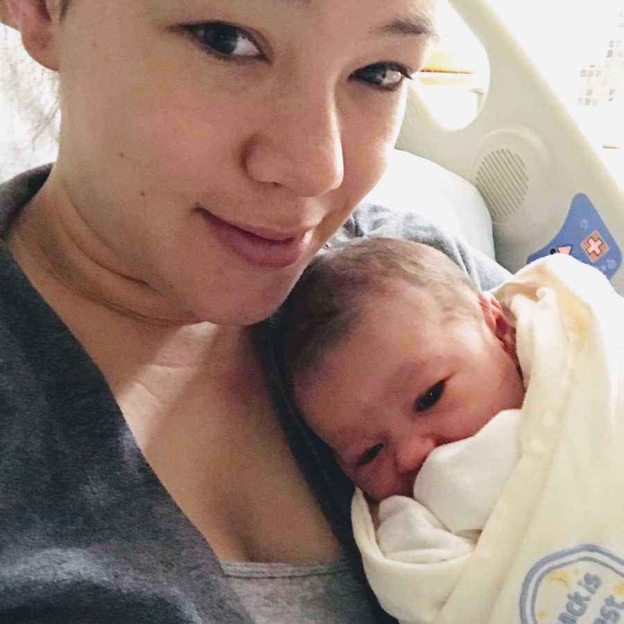 Mother smiles in selfie in hospital bed holding newborn baby to her chest