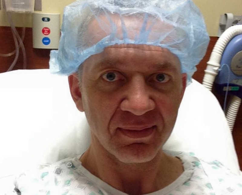 Man with cancer sits in hospital bed with hair net on 