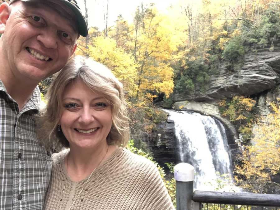 Middle aged couple smiles in selfie with waterfall in background