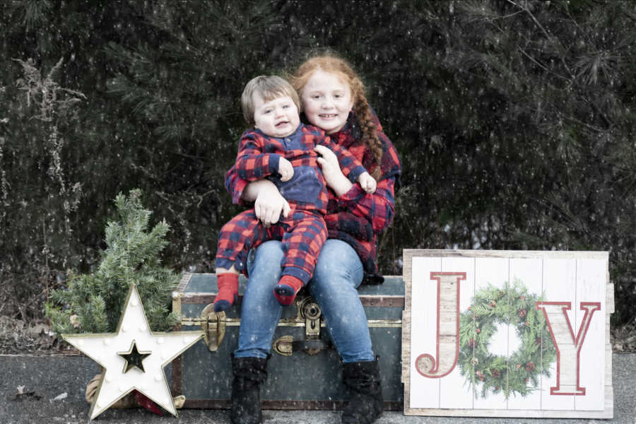 Little girl sits on chest outside with baby brother in her lap in matching outfit