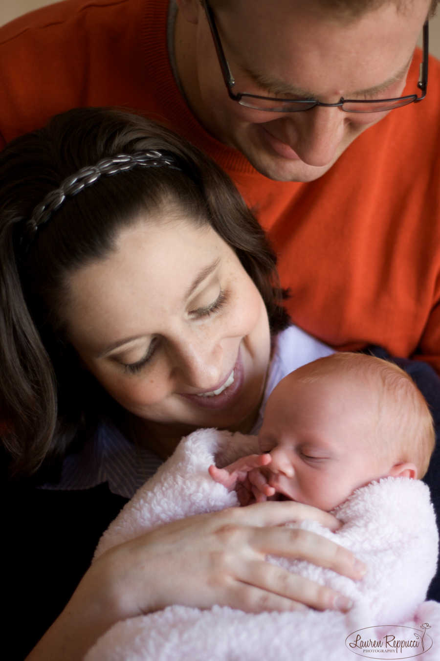 Husband stands behind wife who holds newborn swaddled in blanket