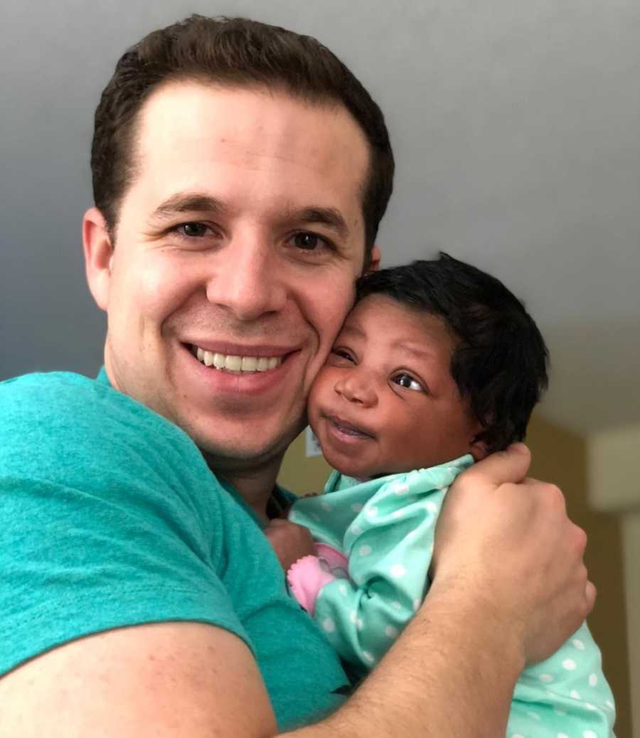 Father smiles as he holds adopted baby girl up to his face