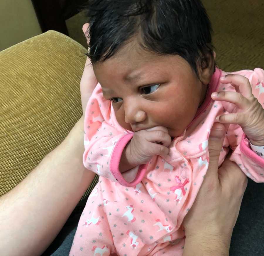 Adopted baby girl sits in lap of parent holding hand to her mouth