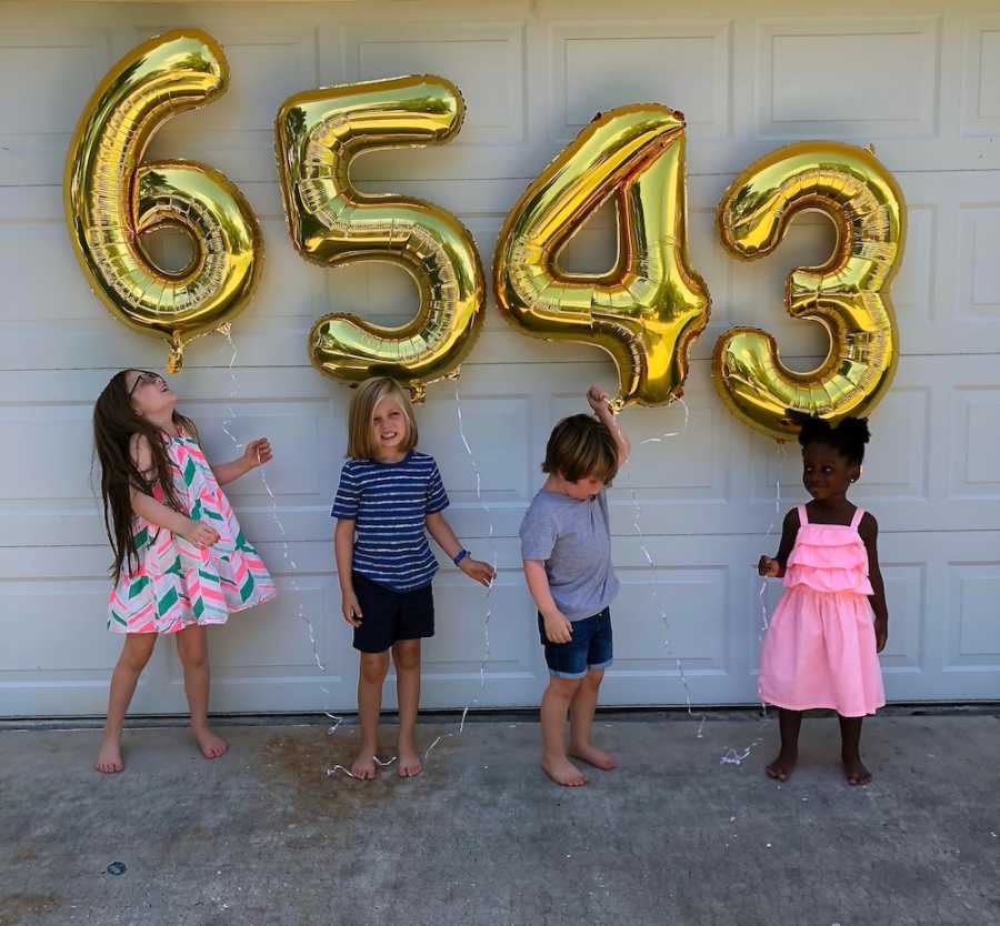 Four siblings stand in front of garage door holding gold ballon that is the number of their age