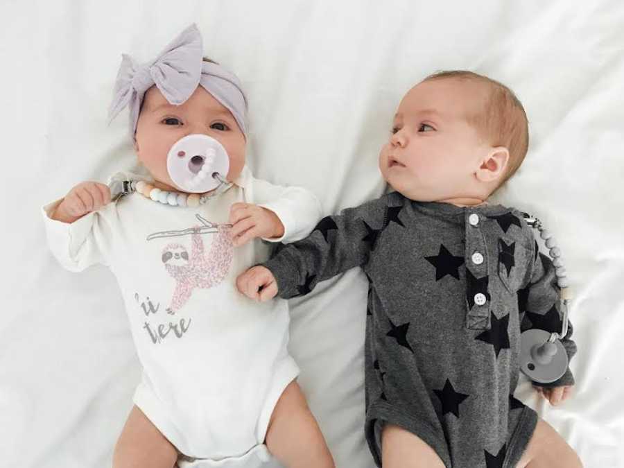 Newborn twins home from NICU lay on their backs in onesies beside each other