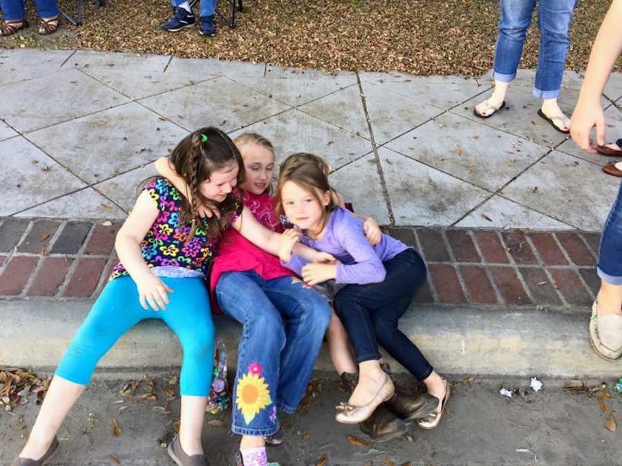Four children hugging on side of curb as they watch parade