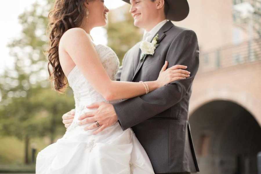 Bride and groom stand with arms around each other as they smile 