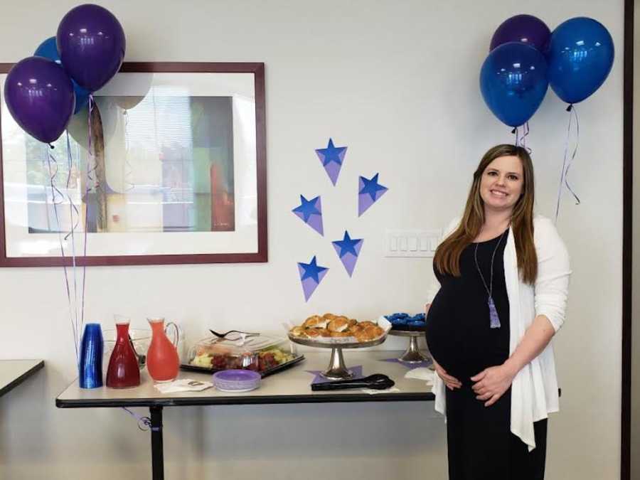 Pregnant woman who struggled with fertility stands beside table of drinks and food at gender reveal for her twins