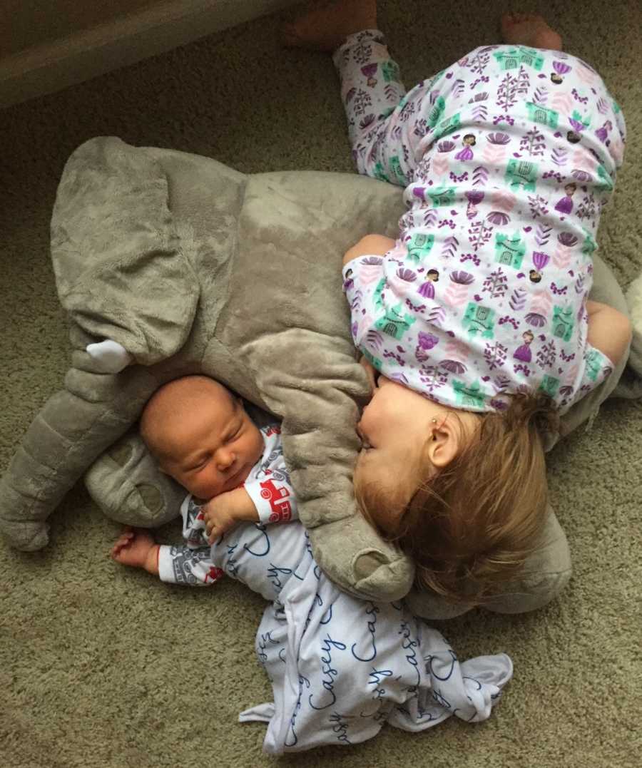 Little girl lays on ground resting on large stuffed animal beside her baby brother