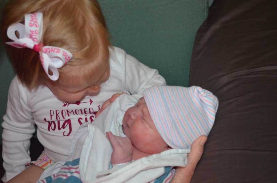 Toddler sits while her new baby sibling is in her lap