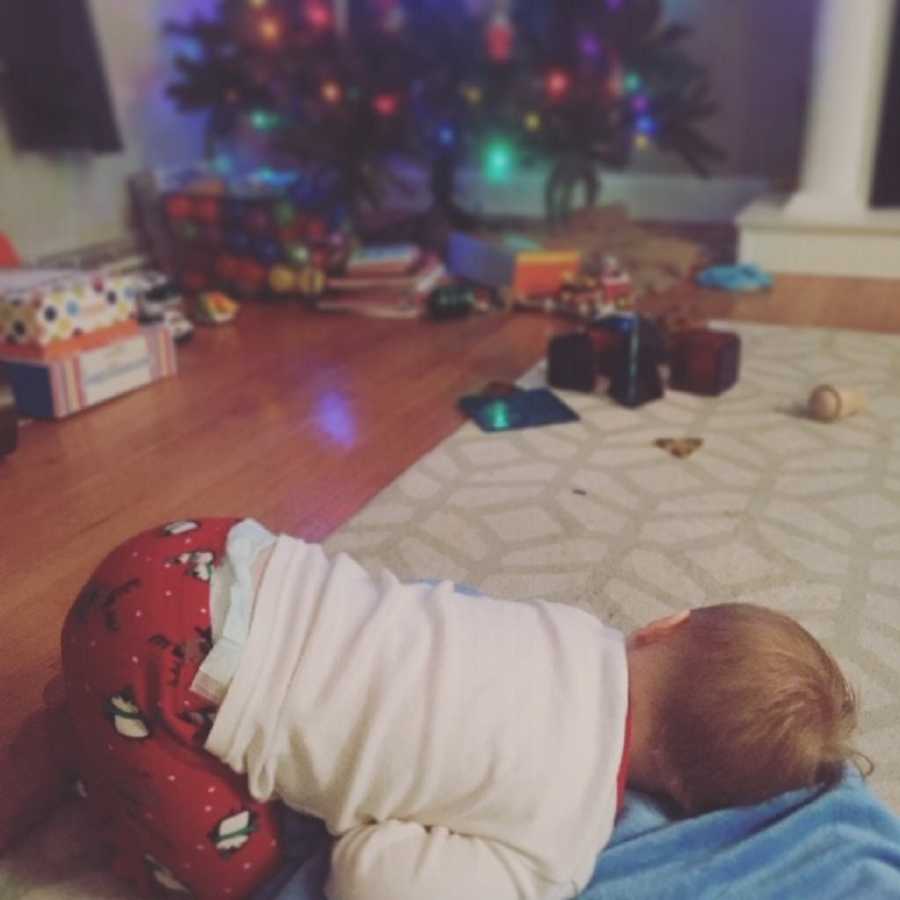 Little boy with down syndrome lays on floor with toys and Christmas presents beside Christmas tree