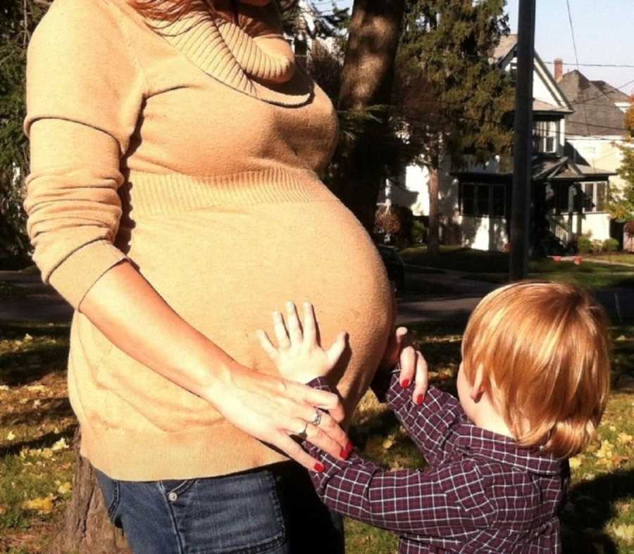 Pregnant woman who had two abortions when she was young stands outside while young boy touches her stomach