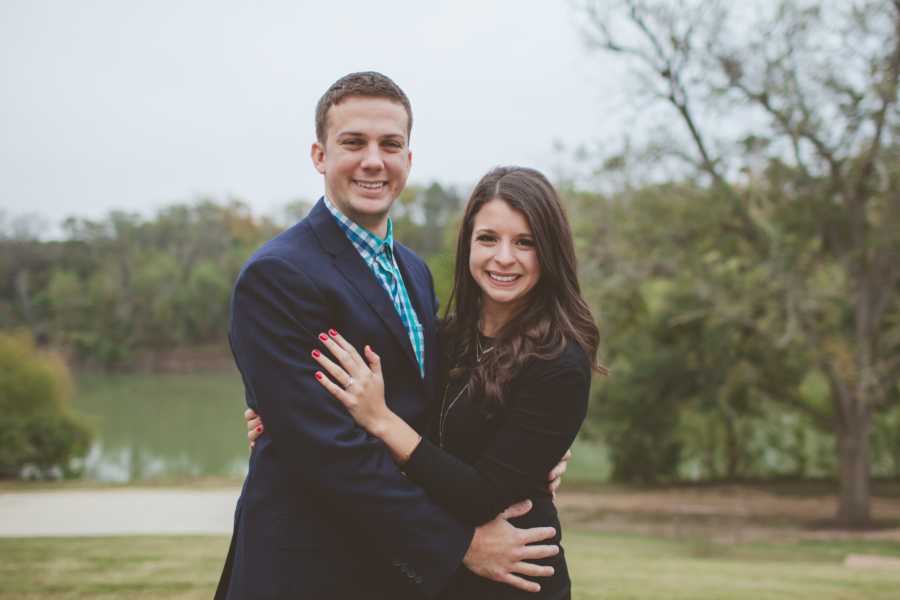 Engaged couple stand outside with arms around each other 