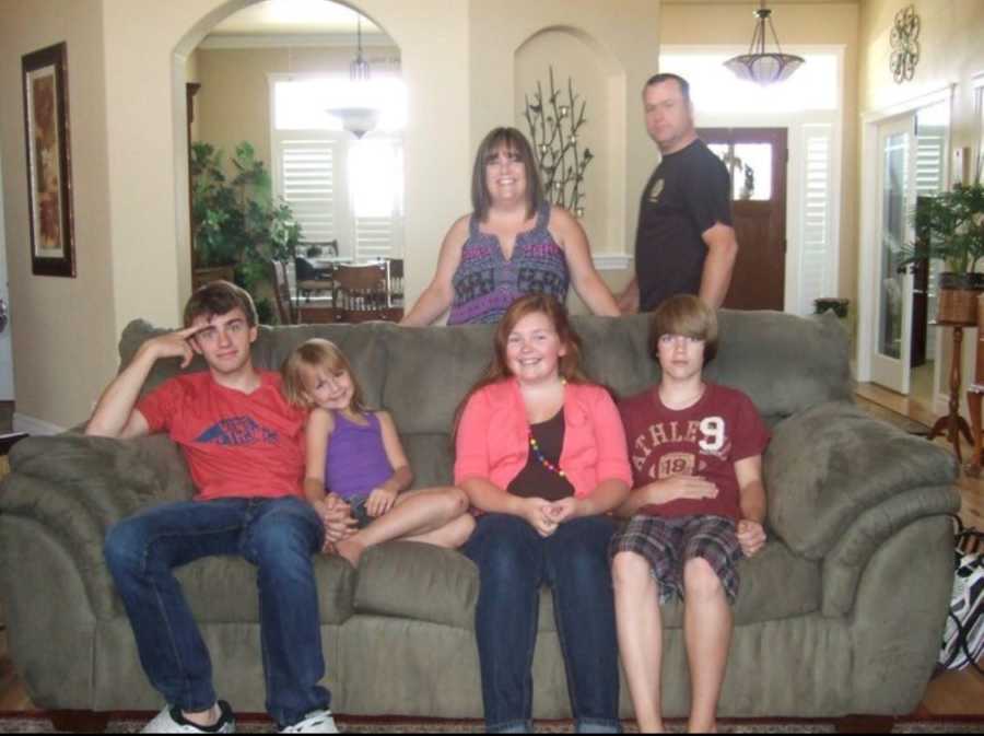 Woman and late husband stand behind couch in home where their four children sit