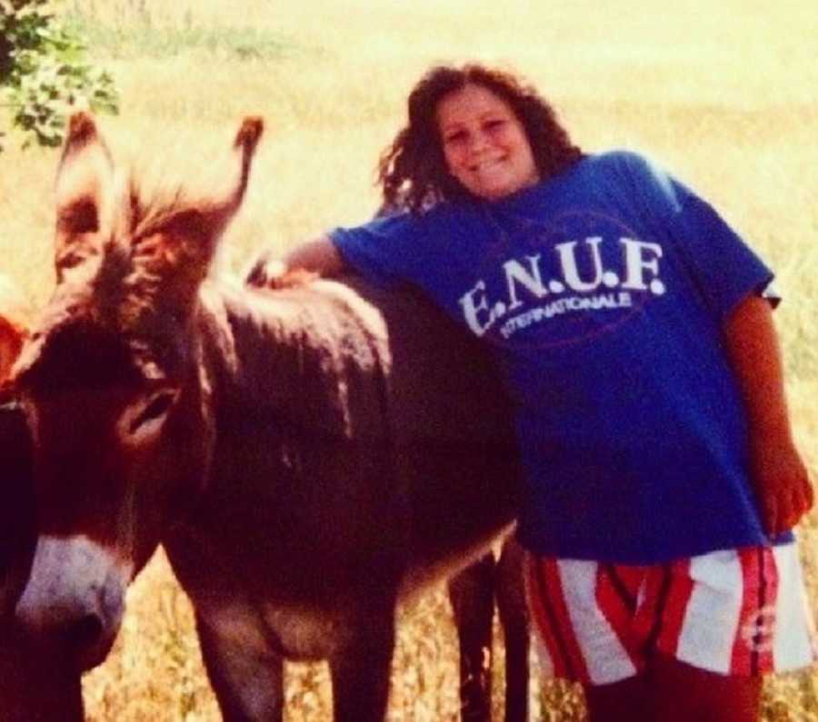 Teen who was bullied for her weight stands smiling beside donkey