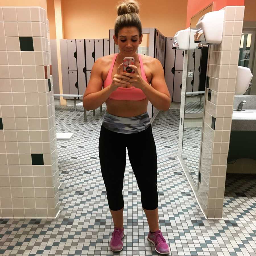 Woman who had eating disorder stands in gym locker room taking mirror selfie at healthy weight