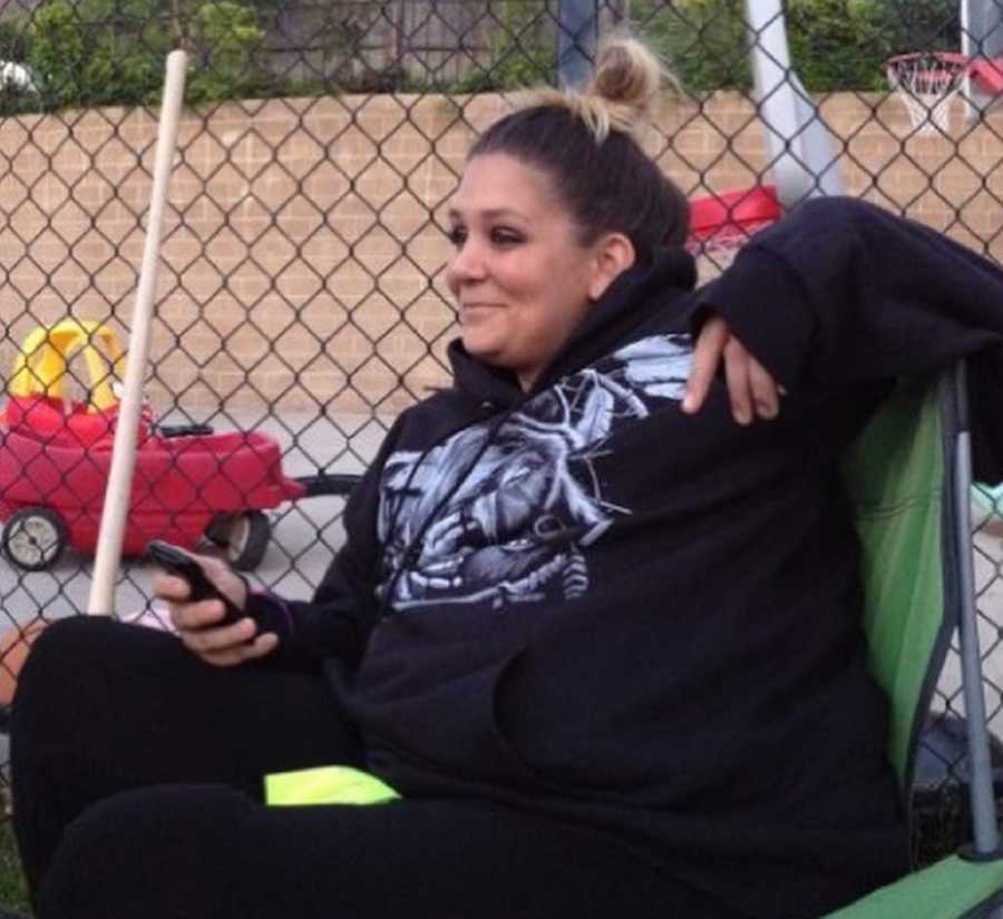 Woman who struggled with eating disorder and gained weight back smiles as she sits in folding chair beside fence