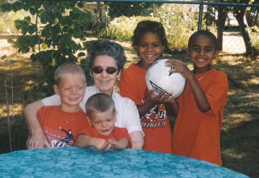 Late grandmother smiles as she sits at table outside with four children in matching orange t-shirts