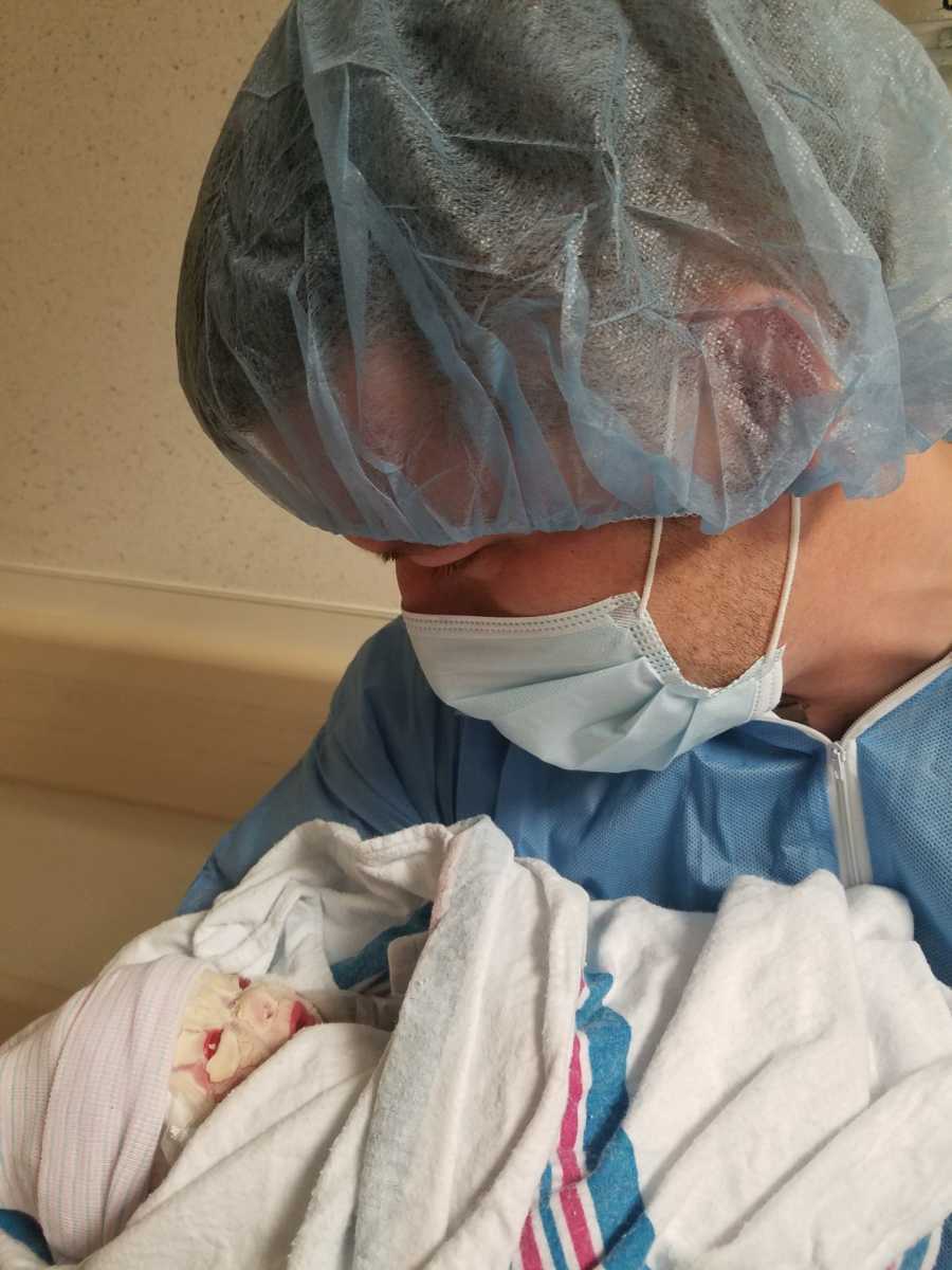 Father with mask and hair net on looks down at newborn in his arms with Harlequin Ichthyosis