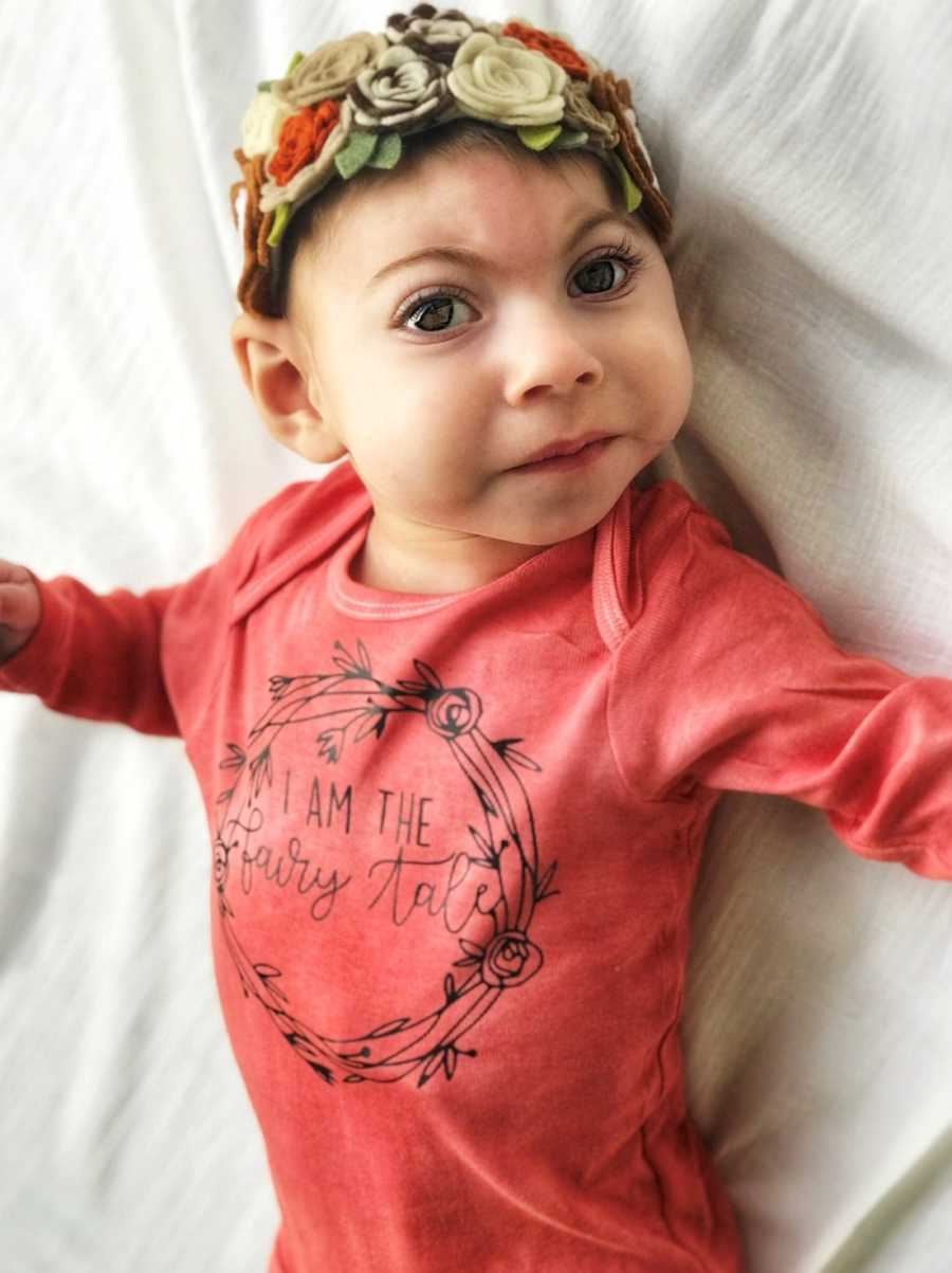 Baby girl with Lissencephaly lays on her back in red onesie with hat with flowers on