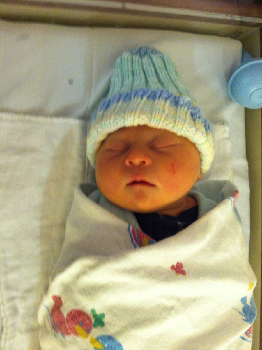 Newborn baby whose mother thinks has down syndrome lays asleep with blue hat on and swaddled in blanket