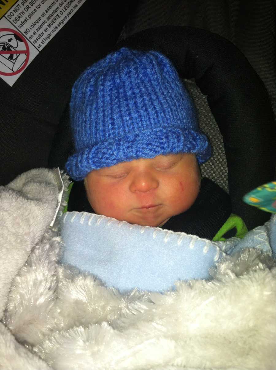 Newborn with down syndrome sleeps in carseat with blue hat on covered in blue and white blankets